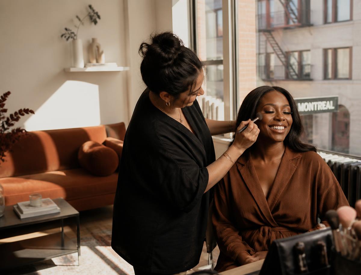 Makeup artist applying makeup to a smiling client in her Montreal living room
